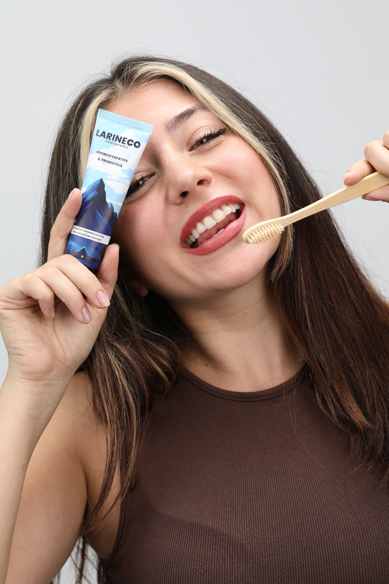 Smiling woman holding Larineco toothpaste tube and bamboo toothbrush